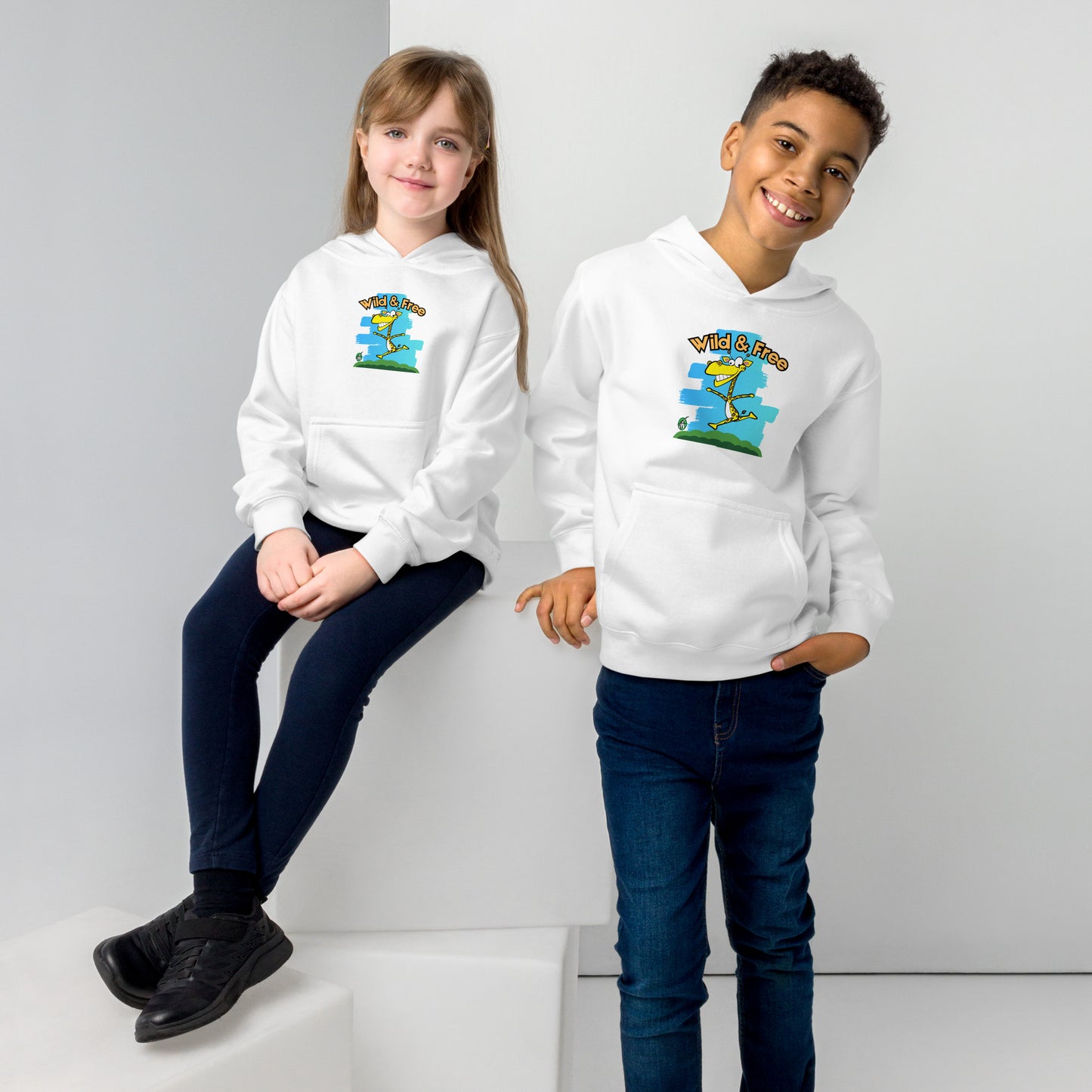 A boy and girl wearing a Wizard Prints kids hoodie in white with a printed graphic on the front of a giraff with the words, Wild and Free.