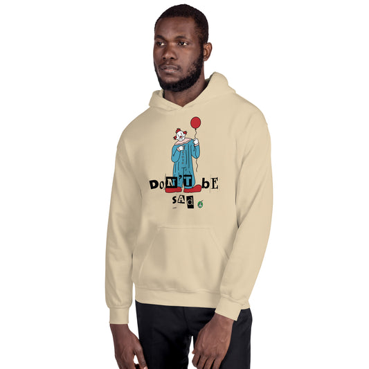 A man standing and wearing a sand beige hoodie with a printed graphic of a clown holding a balloon with the words, 'Don't Be Sad'. Designed by Wizard Prints.