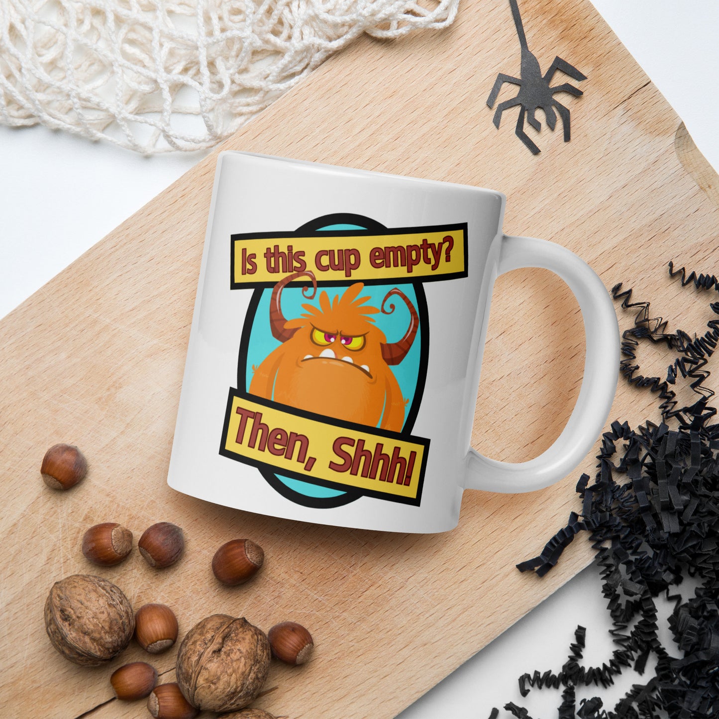 White Wizard Prints funny mug with cartoon monster and 'Is this cup empty? Then Shhh!' text on a wooden board with nuts and spider decorations.