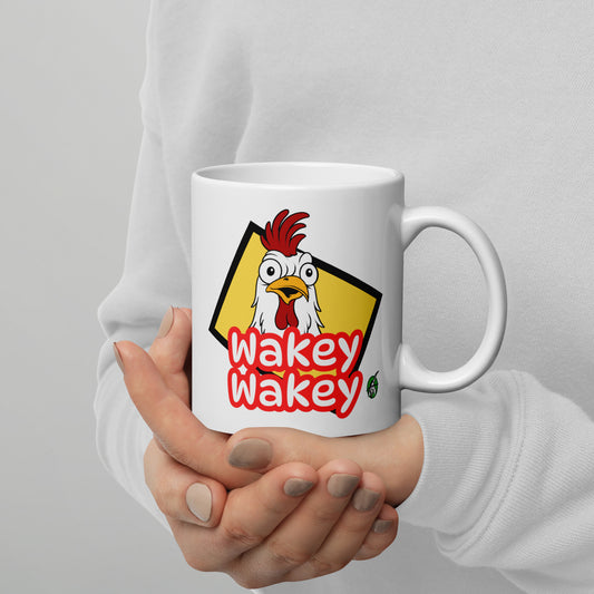 A Wizard Prints white mug with a cartoon rooster graphic and 'Wakey Wakey' text held by a person against a grey background.