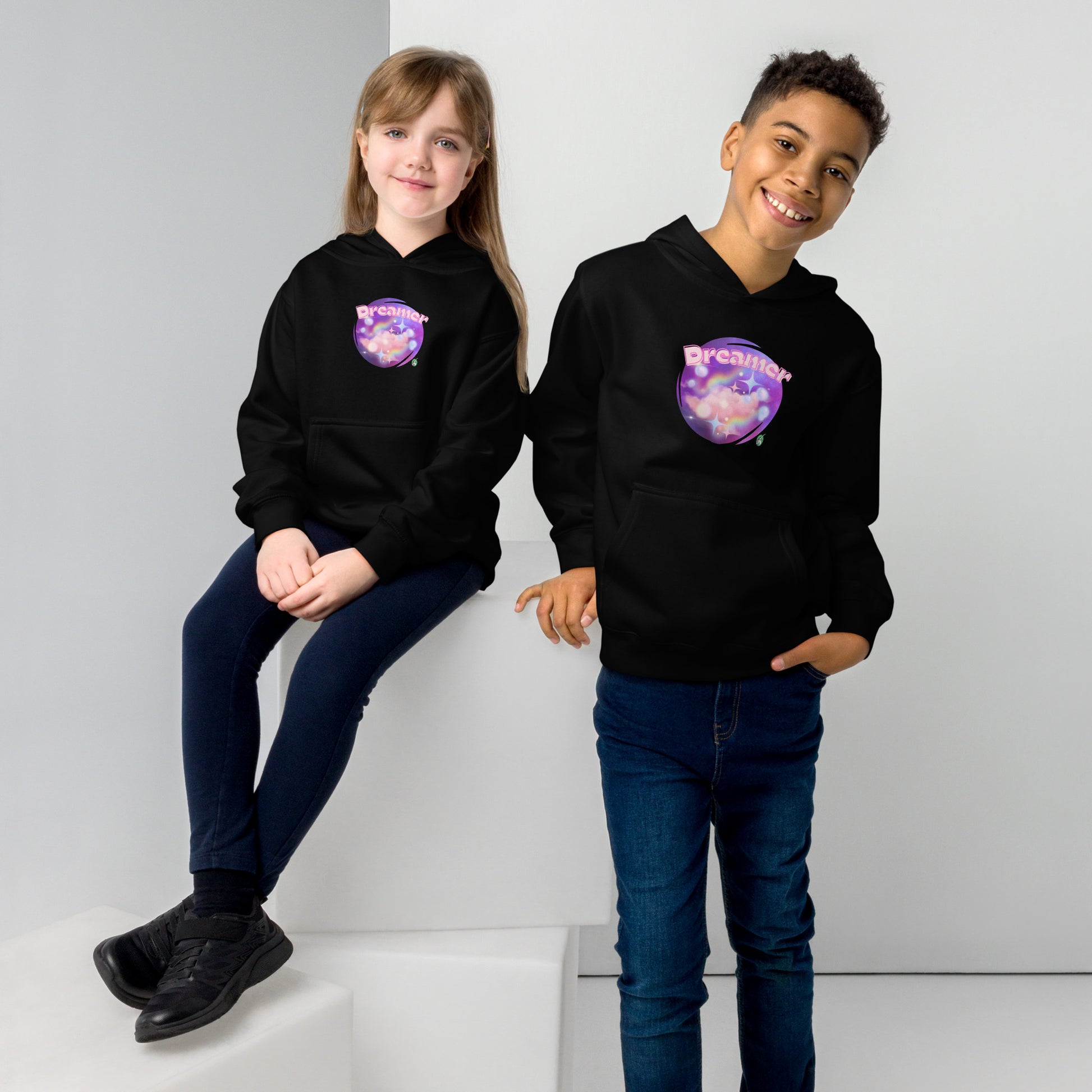 A boy standing and a girl sitting both wearing a black kids graphic hoodie with dreamy purple cirlcle and the word Dreamer by Wizard Prints
