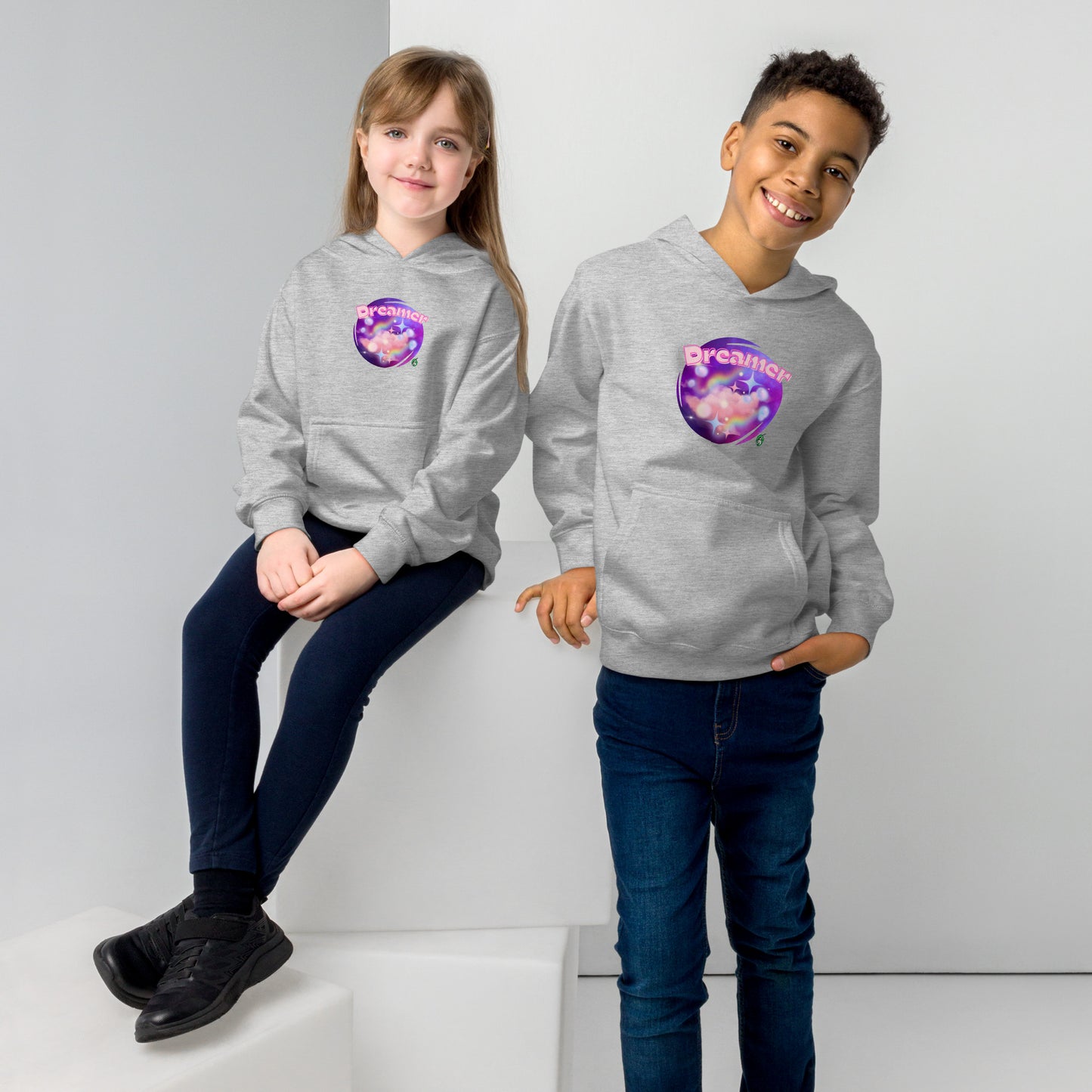 A boy standing and a girl sitting both wearing a grey kids graphic hoodie with dreamy purple cirlcle and the word Dreamer by Wizard Prints
