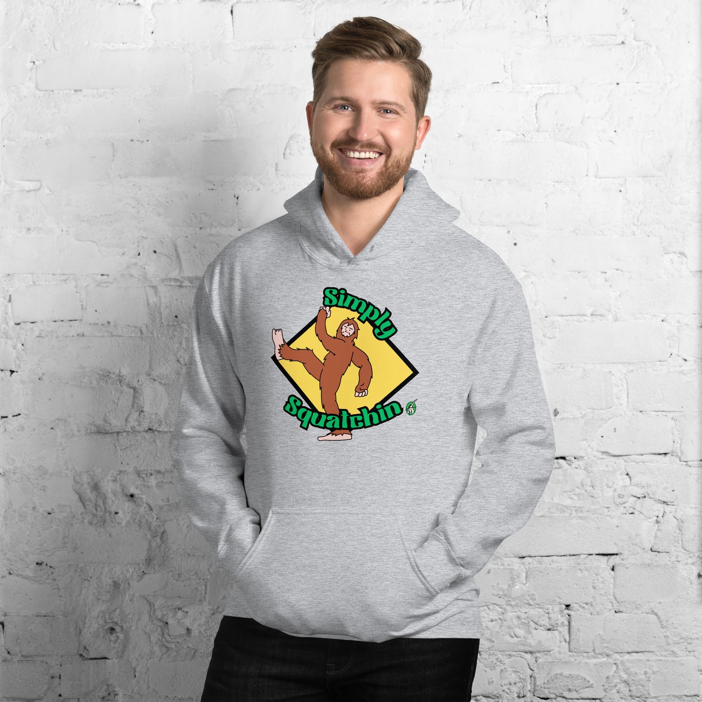 A man standing and wearing a grey hoodie with a printed graphic of a sasquatch with the words, Simply Squatchin. Designed by Wizard Prints.