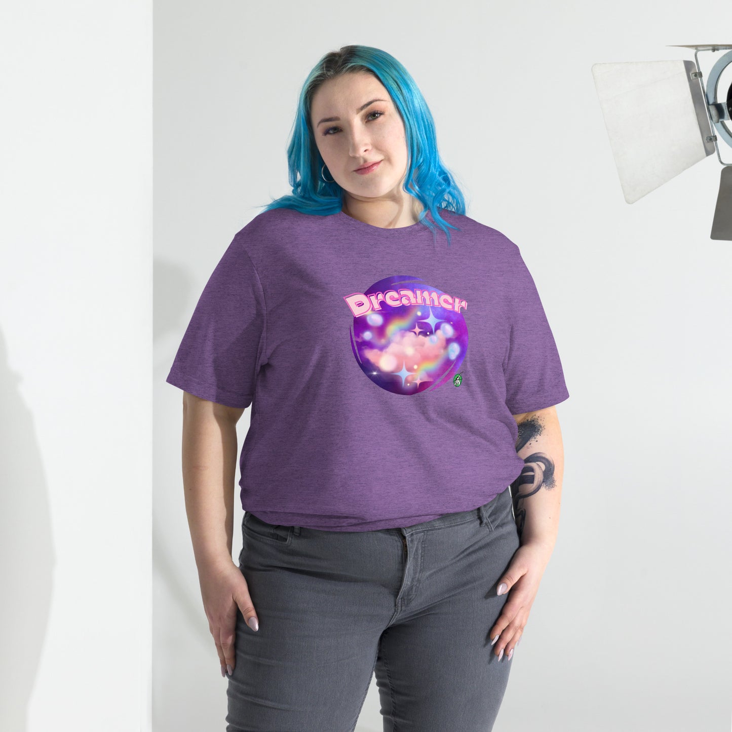 A woman standing wearing a purple tee shirt with a printed graphic of a galaxy background and the word Dreamer on top. Designed by Wizard Prints
