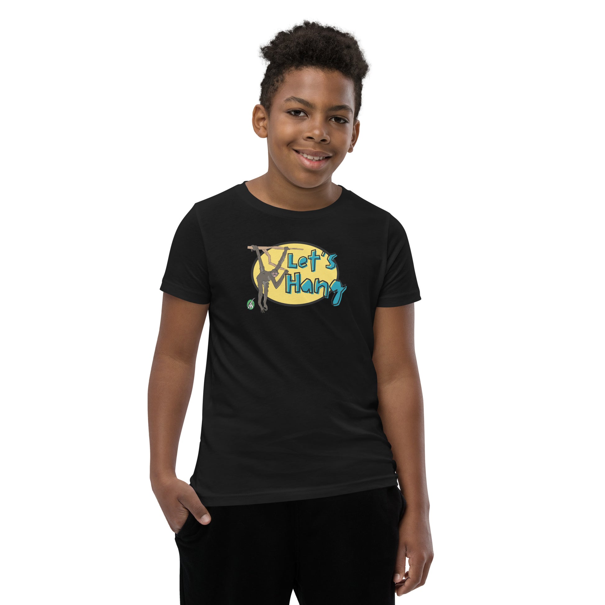 A boy standing wearing a black graphic tee shirt with a funny graphic on the front of a monkey hanging from the tree branch saying, Let's Hang by Wizard Prints and jeans on a white background
