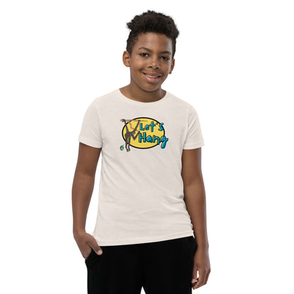 A boy standing wearing a cream graphic tee shirt with a funny graphic on the front of a monkey hanging from the tree branch saying, Let's Hang by Wizard Prints and jeans on a white background
