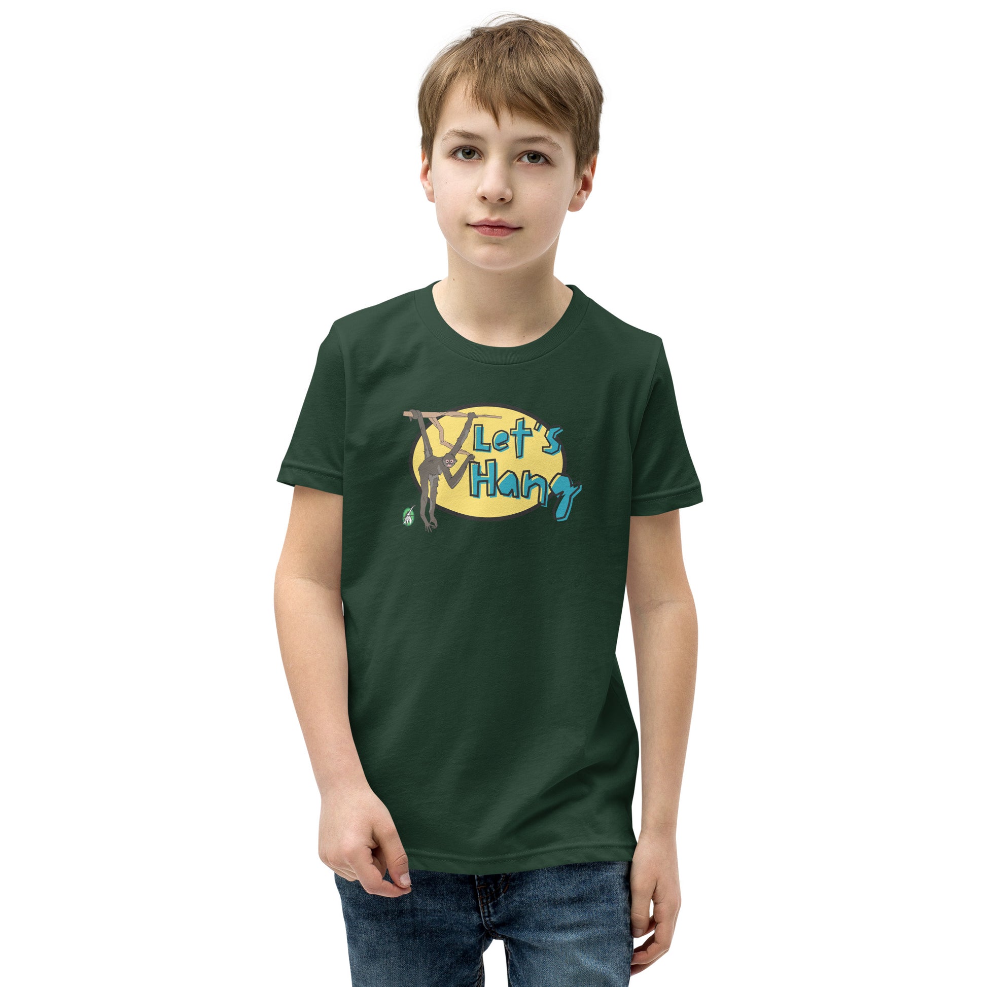 A boy standing wearing a green graphic tee shirt with a funny graphic on the front of a monkey hanging from the tree branch saying, Let's Hang by Wizard Prints and jeans on a white background
