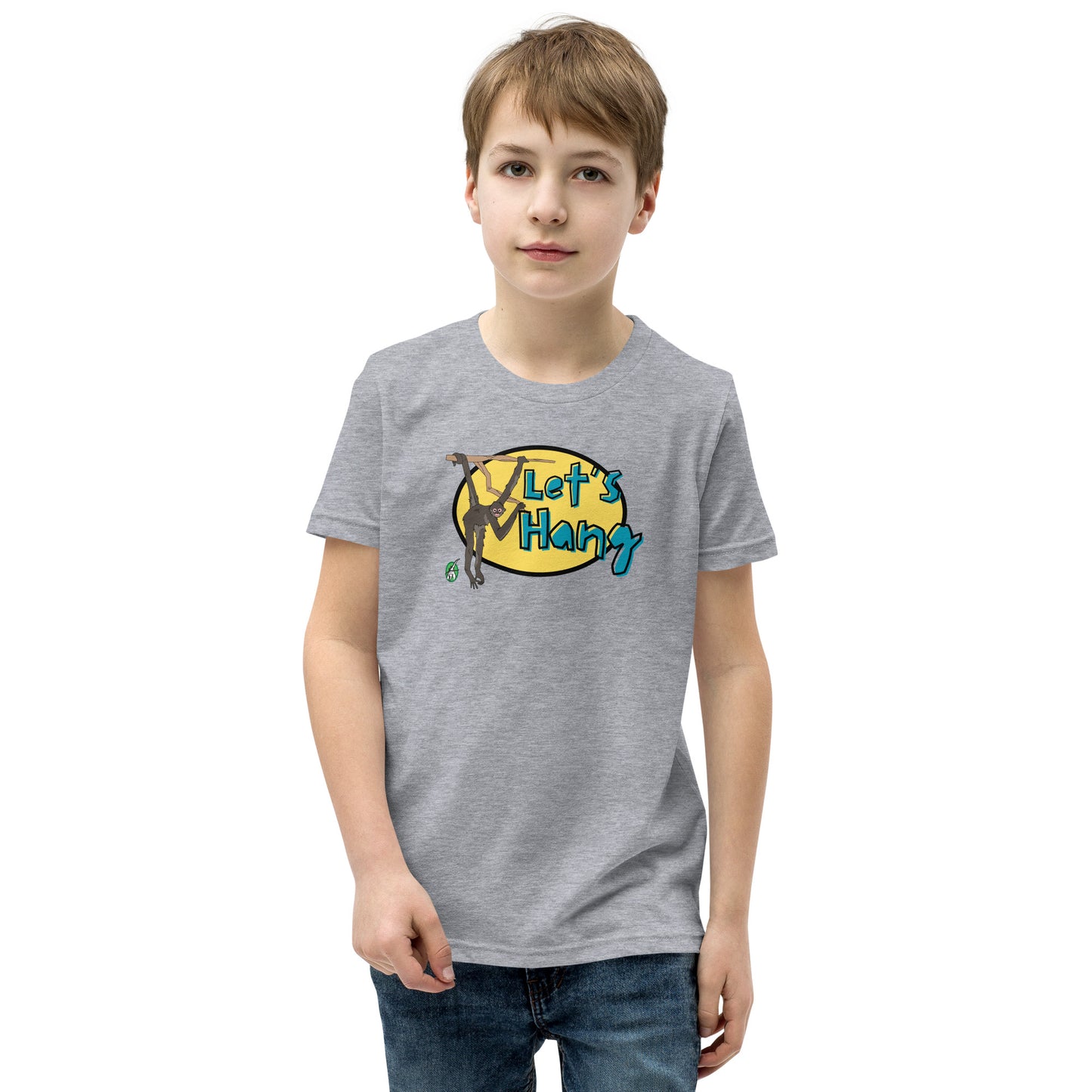 A boy standing wearing a grey graphic tee shirt with a funny graphic on the front of a monkey hanging from the tree branch saying, Let's Hang by Wizard Prints and jeans on a white background

