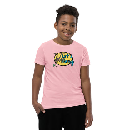 A boy standing wearing a pink graphic tee shirt with a funny graphic on the front of a monkey hanging from the tree branch saying, Let's Hang by Wizard Prints and jeans on a white background
