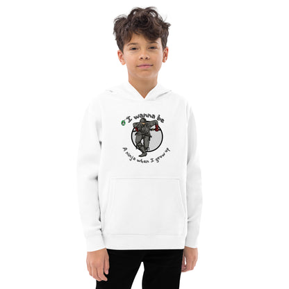 A boy standing wearing a white kids graphic hoodie with a ninja and the words I wanna be a ninja when I grow up, by Wizard Prints