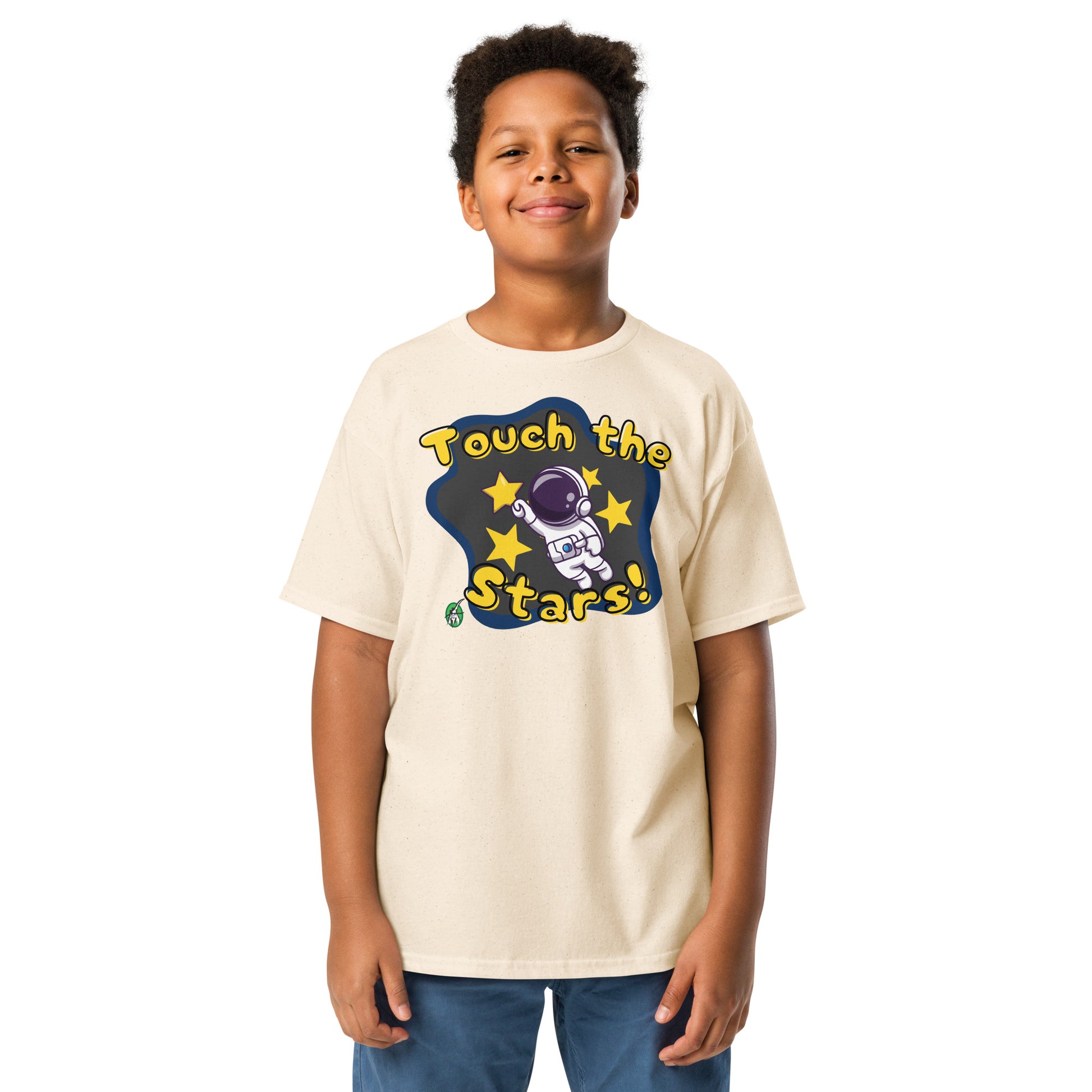 A boy standing and wearing a beige t-shirt featuring a printed graphic of a cartoon astronaut and the words, 'Touch the Stars'. Designed by Wizard Prints.