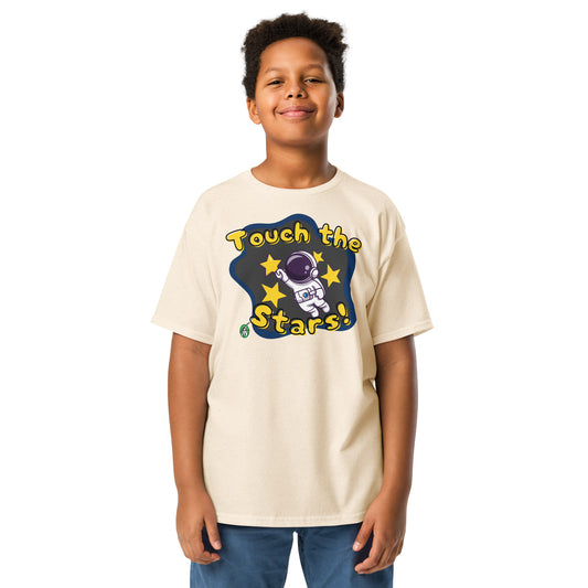 A boy standing and wearing a beige t-shirt featuring a printed graphic of a cartoon astronaut and the words, 'Touch the Stars'. Designed by Wizard Prints.