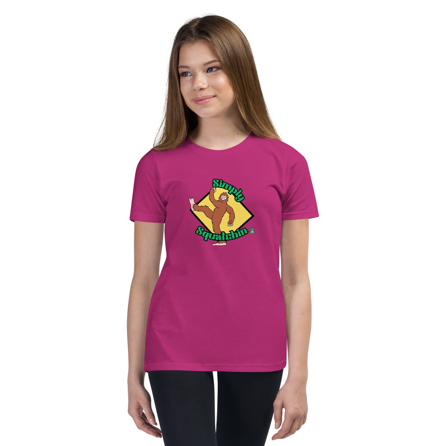 A girl standing wearing a berry pink graphic t-shirt with a brown sasquatch and the statement, Simply Squatchin on a yellow background, by Wizard Prints