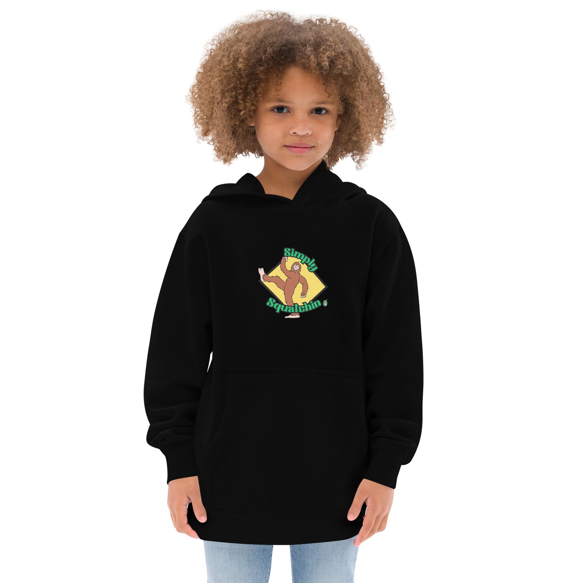 A girl standing wearing a black kids graphic hoodie with a brown sasquatch and the statement, Simply Squatchin on a yellow background, by Wizard Prints