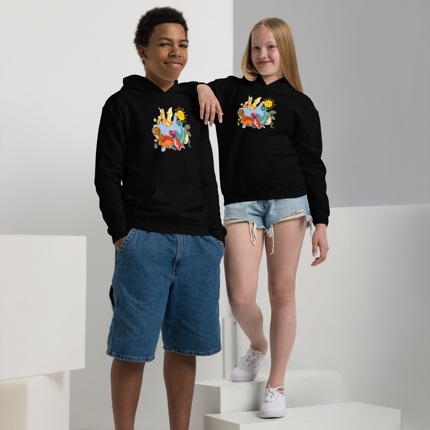 A boy and girl wearing a Wizard Prints kids hoodie in black with a printed graphic on the front of a  group of cartoon dinosaurs
