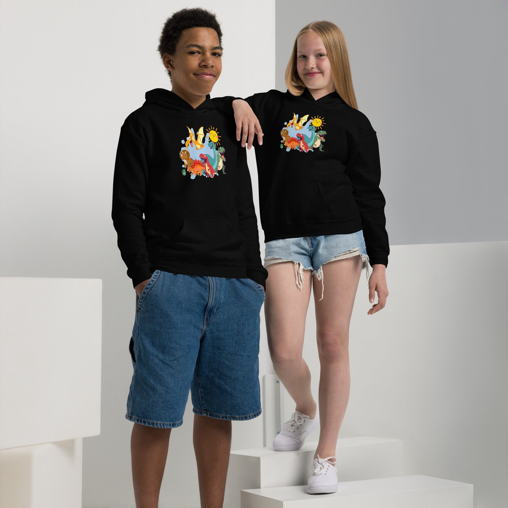 A boy and girl wearing a Wizard Prints kids hoodie in black with a printed graphic on the front of a  group of cartoon dinosaurs
