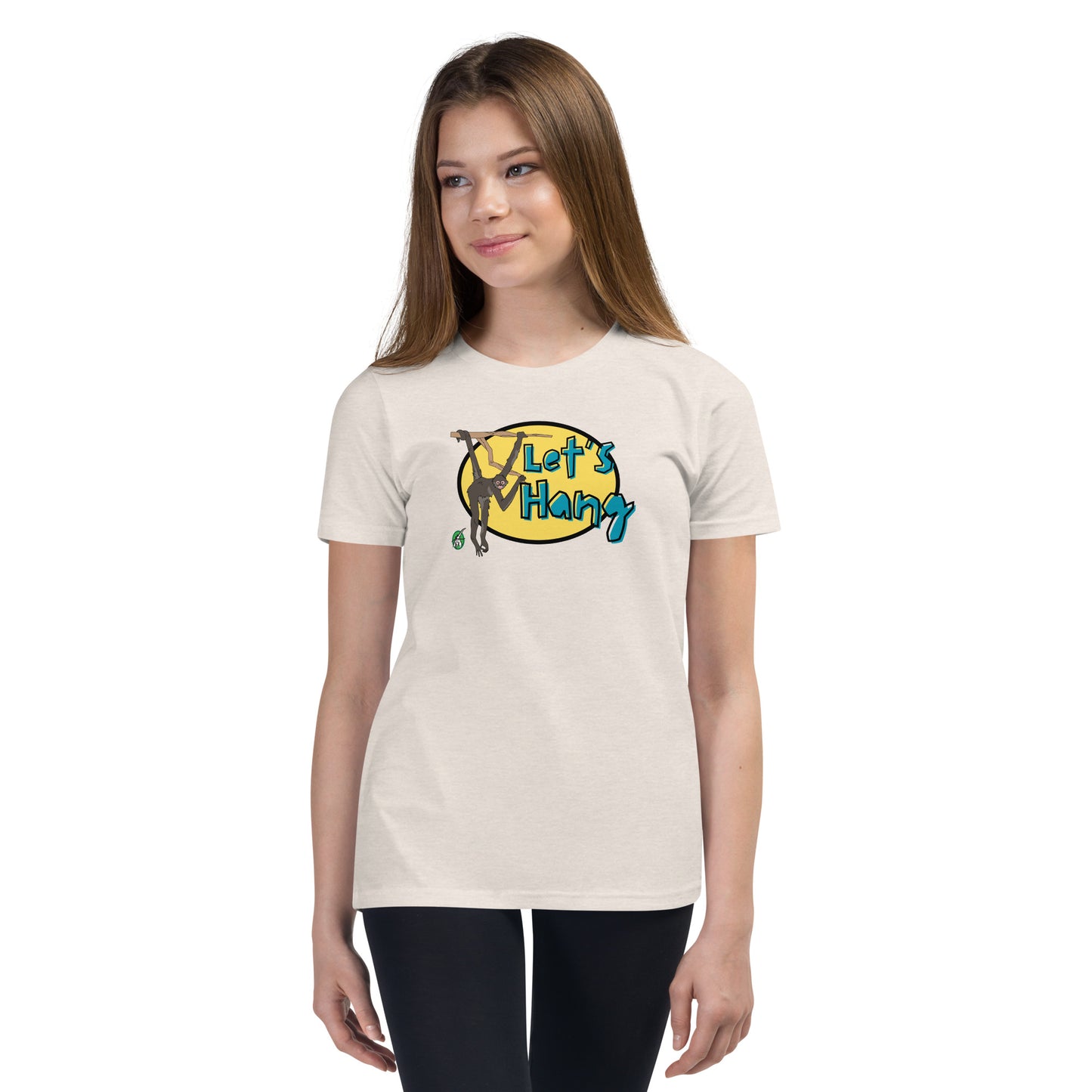 A girl standing wearing a cream graphic tee shirt with a funny graphic on the front of a monkey hanging from the tree branch saying, Let's Hang by Wizard Prints and jeans on a white background