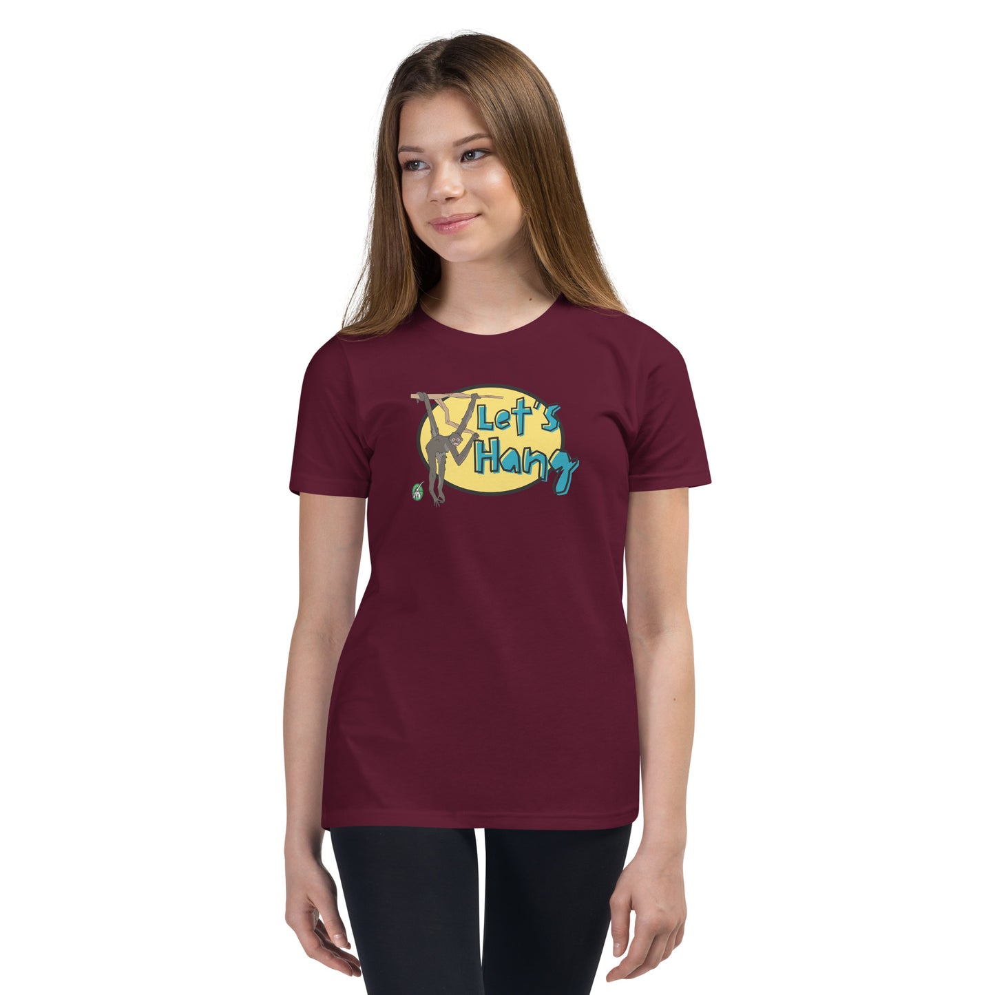 A girl standing wearing a dark red graphic tee shirt with a funny graphic on the front of a monkey hanging from the tree branch saying, Let's Hang by Wizard Prints and jeans on a white background
