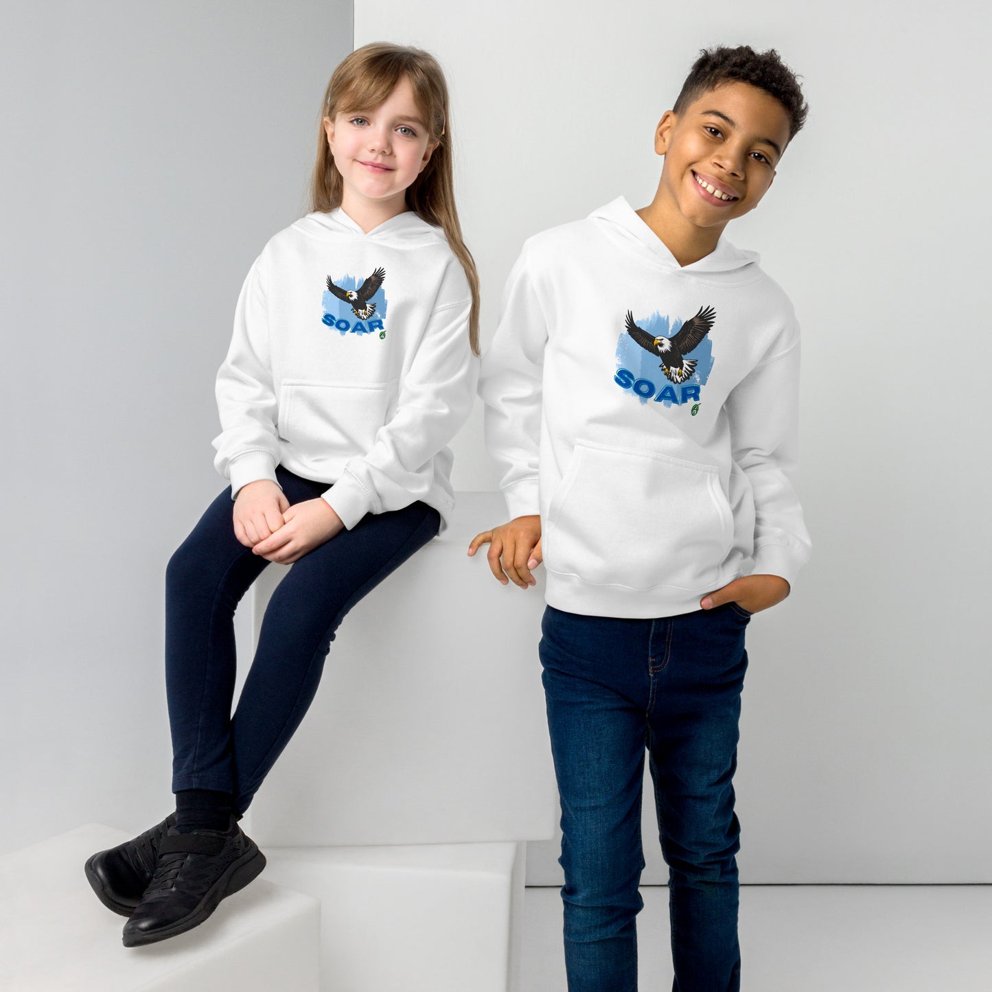 A boy and girl wearing a Wizard Prints kids hoodie in white with a printed graphic on the front of an eagle soaring in the sky.