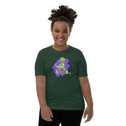  A girl standing wearing a forest green kids t-shirt with the printed graphic of a cartoon dinosaur and the word, Smile. Designed by Wizard Prints