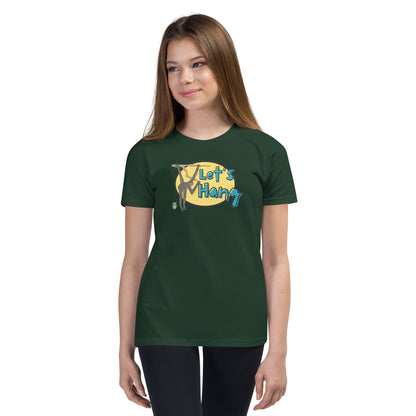 A girl standing wearing a green graphic tee shirt with a funny graphic on the front of a monkey hanging from the tree branch saying, Let's Hang by Wizard Prints and jeans on a white background
