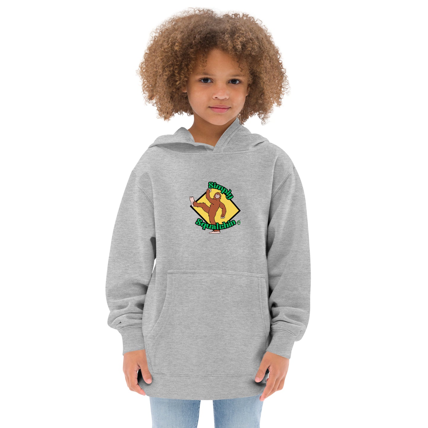 A girl standing wearing a grey kids graphic hoodie with a brown sasquatch and the statement, Simply Squatchin on a yellow background, by Wizard Prints