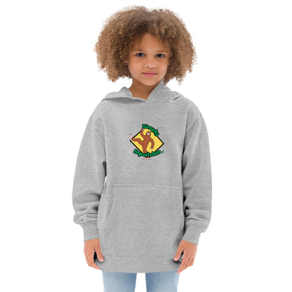 A girl standing wearing a grey kids graphic hoodie with a brown sasquatch and the statement, Simply Squatchin on a yellow background, by Wizard Prints