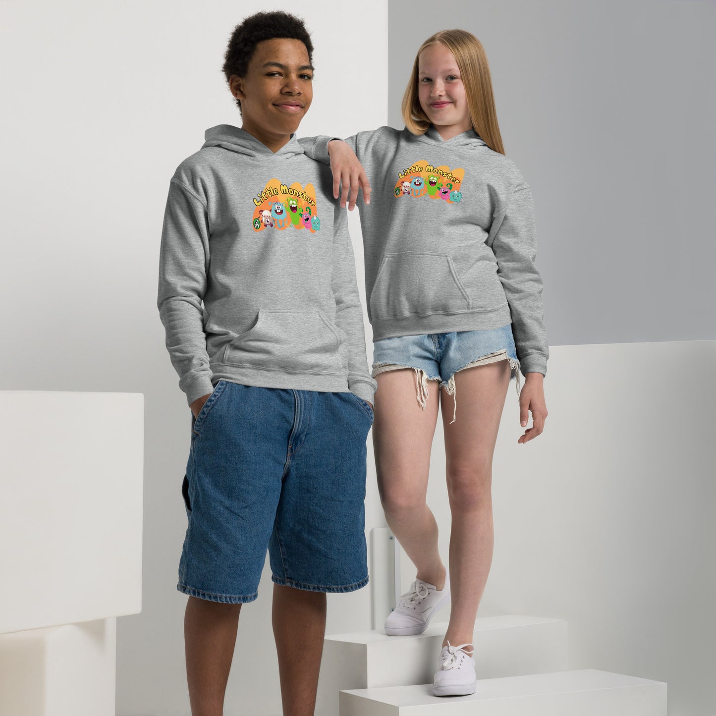 A boy and girl wearing a Wizard Prints kids hoodie in grey with a printed graphic on the front of cartoon characters of monsters with the words, Little Monsters 