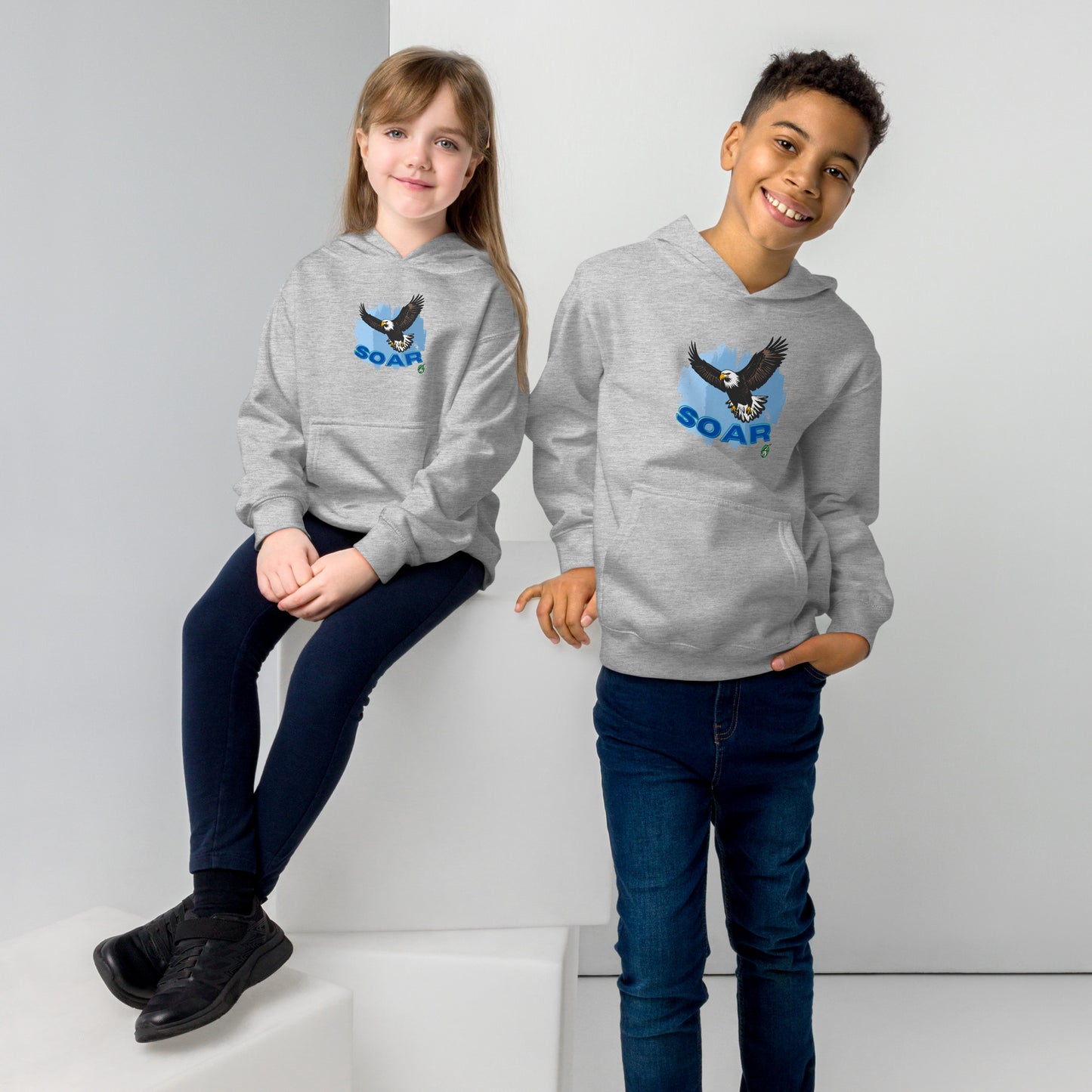 A boy and girl wearing a Wizard Prints kids hoodie in grey with a printed graphic on the front of an eagle soaring in the sky.