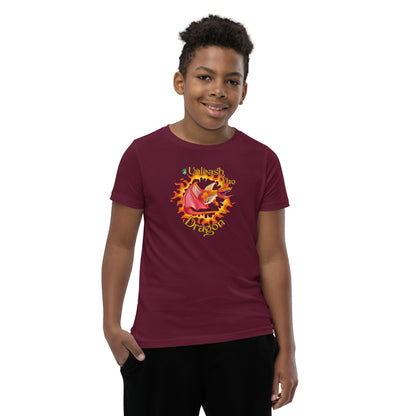  A boy standing wearing a maroon kids t-shirt with the printed graphic of a fire-breathing dragon with the statement, Unleash the Dragon. Designed by Wizard Prints