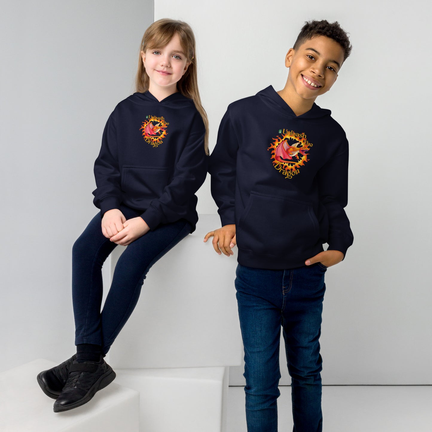  A boy standing and a girl sitting both wearing a navy blue kids graphic hoodie with a red dragon breathing fire and the statement unleash the dragon, by Wizard Prints