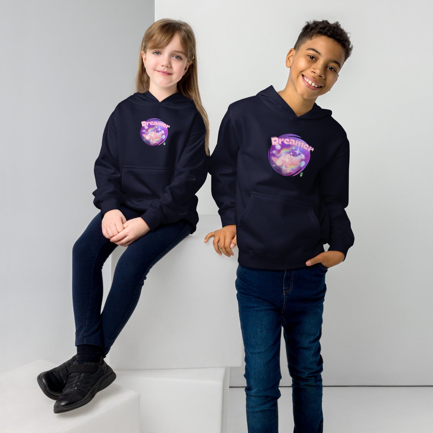 A boy standing and a girl sitting both wearing a navy kids graphic hoodie with dreamy purple cirlcle and the word Dreamer by Wizard Prints
