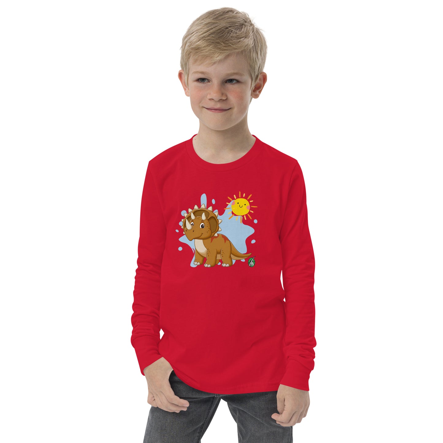 A boy standing wearing a red long sleeve t-shirt with a printed graphic of a smiling triceratops and the sun. Designed by Wizard Prints.