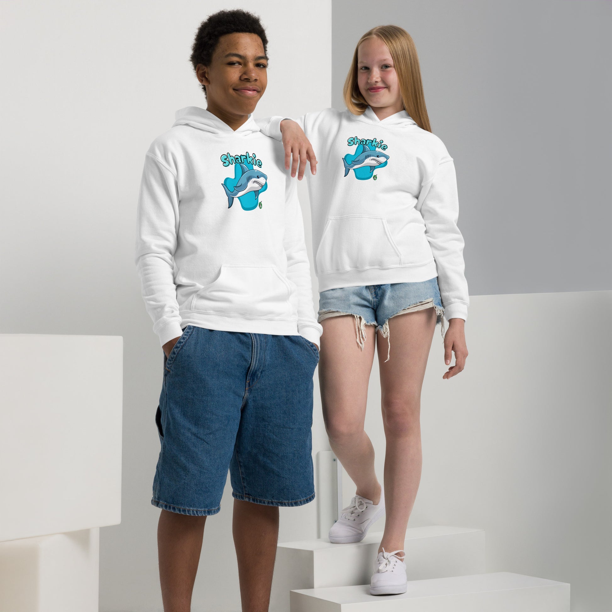A boy and girl wearing a Wizard Prints kids hoodie in white with a printed graphic on the front of a cartoon shark with the words, Sharkie