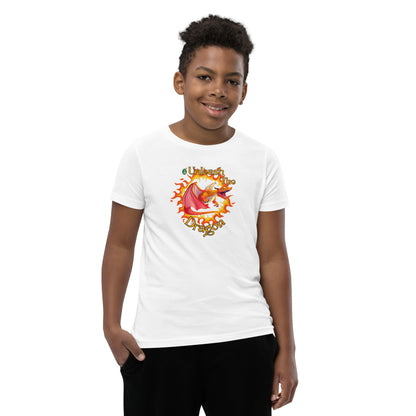  A boy standing wearing a white kids t-shirt with the printed graphic of a fire-breathing dragon with the statement, Unleash the Dragon. Designed by Wizard Prints