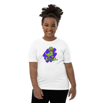  A girl standing wearing a white kids t-shirt with the printed graphic of a cartoon dinosaur and the word, Smile. Designed by Wizard Prints