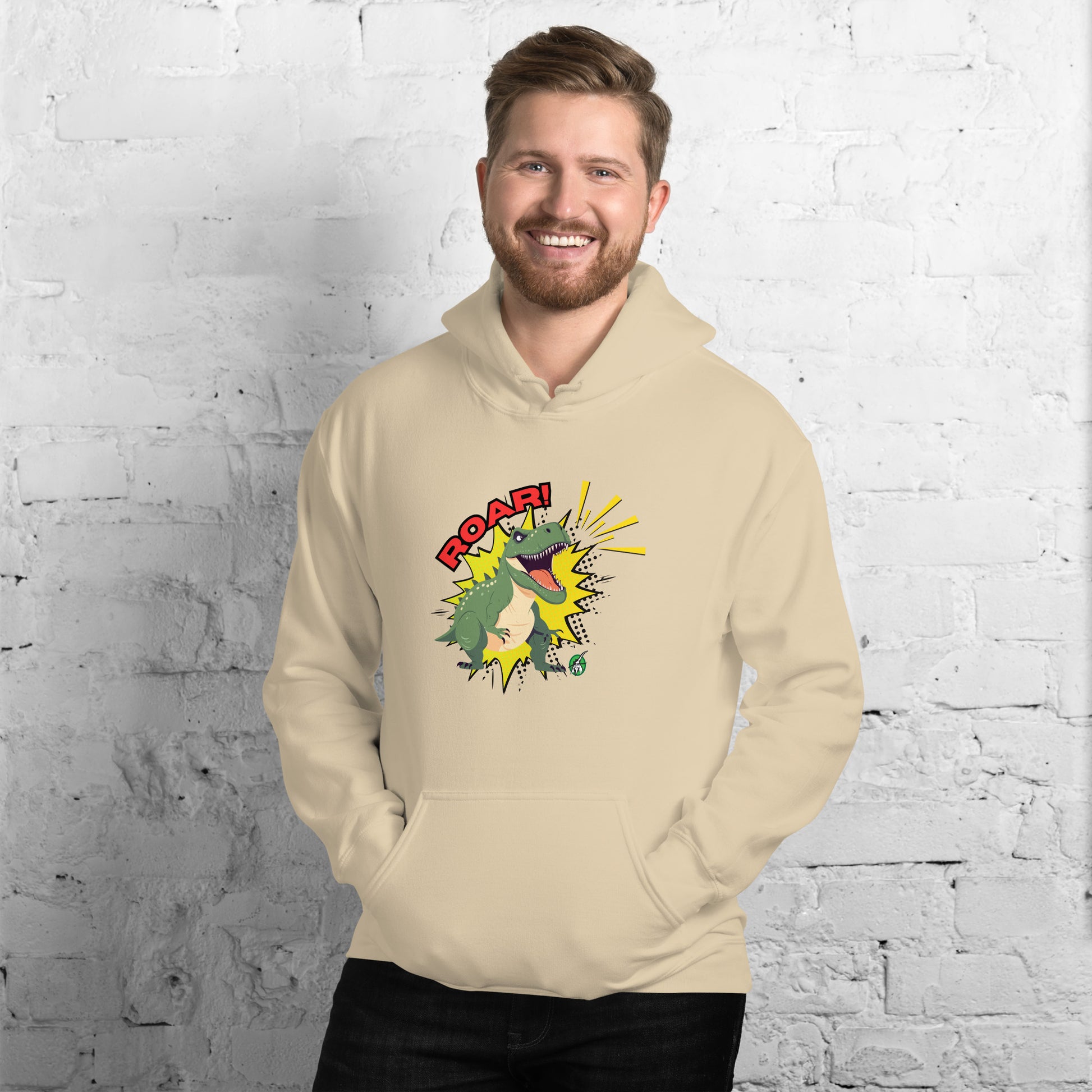 A man standing wearing a beige hoodie with a printed graphic of a green roaring cartoon dinosaur and the word Roar! Designed by Wizard Prints