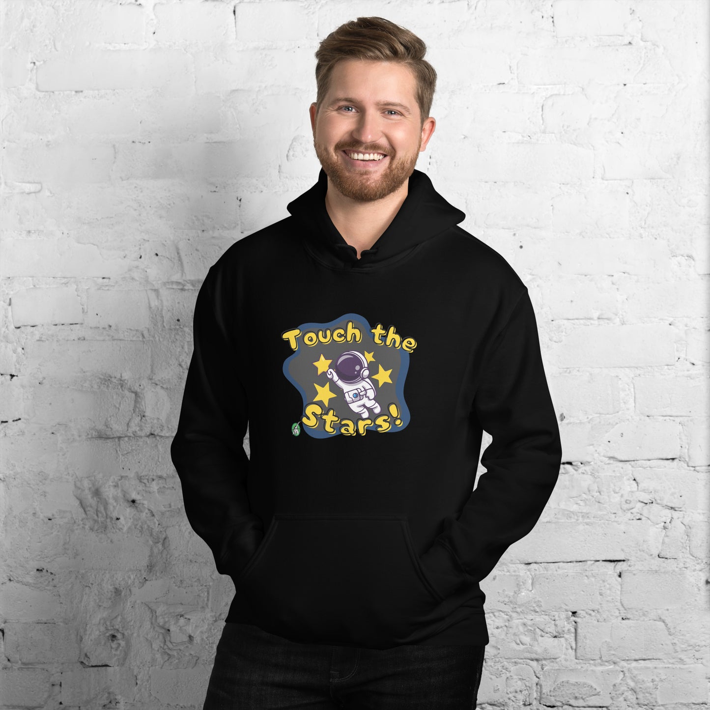 A man standing wearing a black hoodie with a printed graphic of a cartoon astronaut and the words, Touch the Stars. Designed by Wizard Prints.