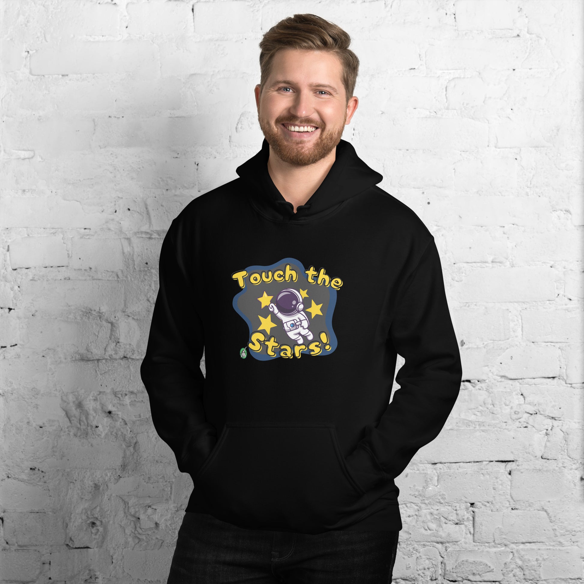 A man standing wearing a black hoodie with a printed graphic of a cartoon astronaut and the words, Touch the Stars. Designed by Wizard Prints.