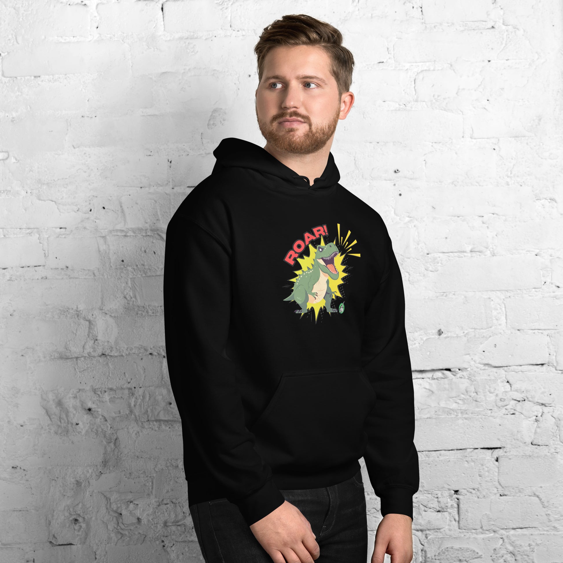 A man standing wearing a black hoodie with a printed graphic of a green roaring cartoon dinosaur and the word Roar! Designed by Wizard Prints