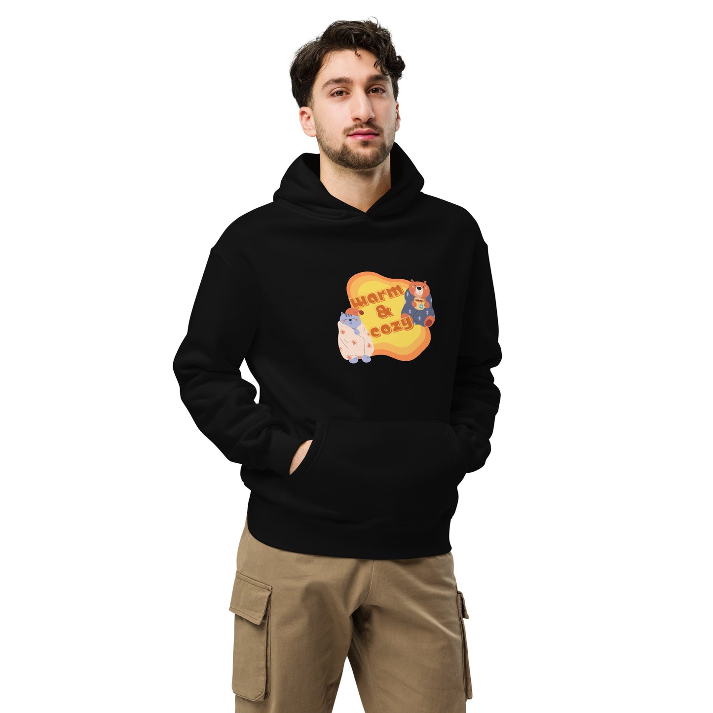 A man standing wearing a black hoodie by Wizard Prints featuring a printed graphic of a cartoon cat and bear wrapped in blankets and the words, Warm & Cozy. 