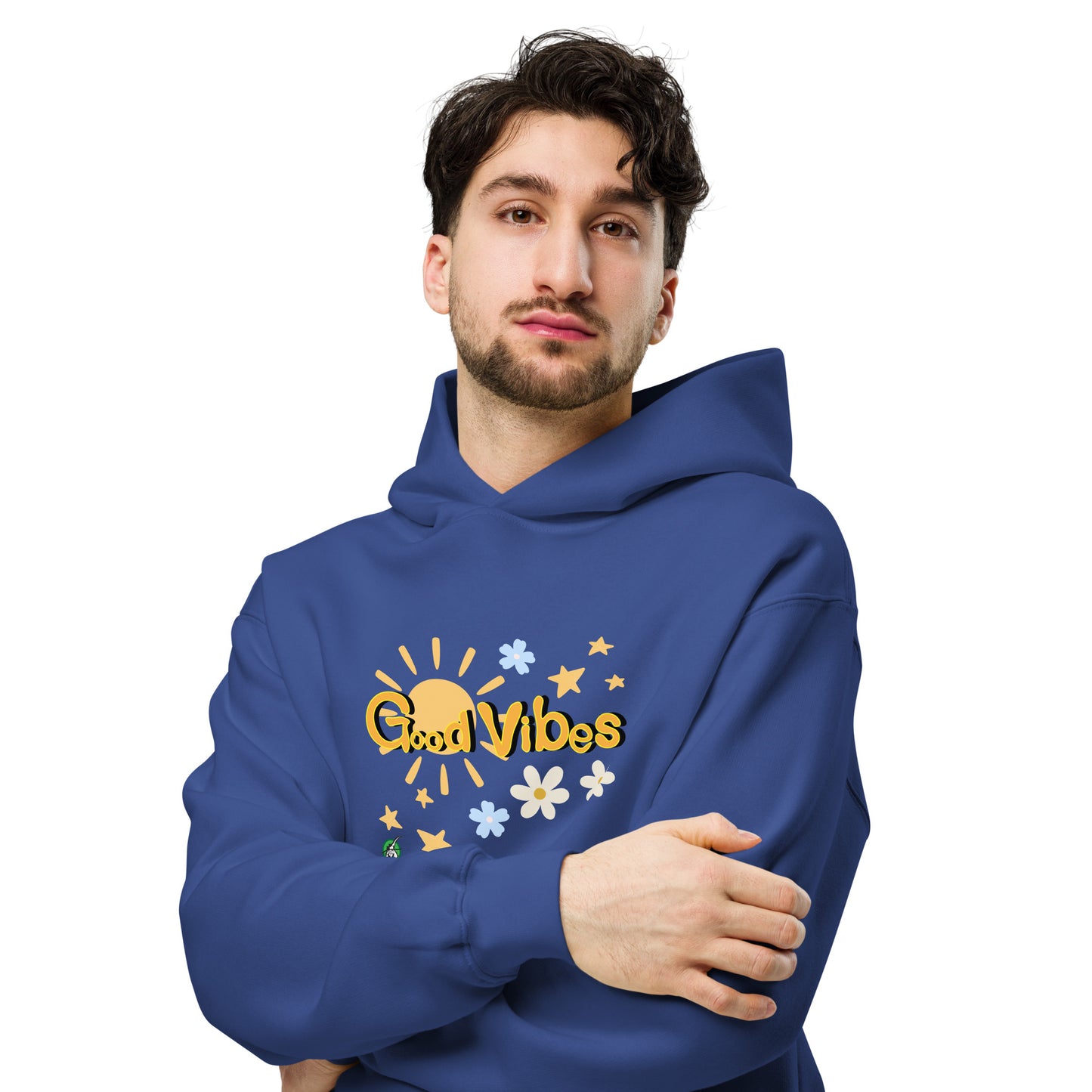 A man standing wearing a blue hoodie by Wizard Prints featuring a printed graphic of the sun, flowers, stars and the words, 'Good Vibes'.