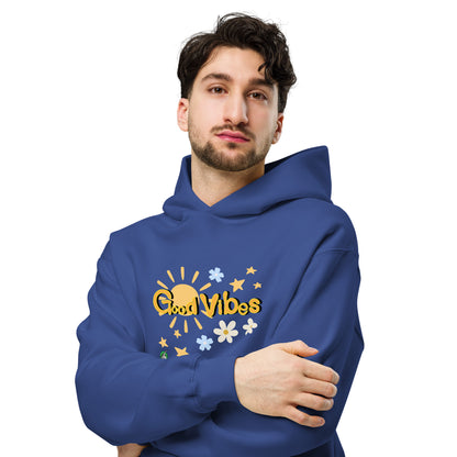 A man standing wearing a blue hoodie by Wizard Prints featuring a printed graphic of the sun, flowers, stars and the words, 'Good Vibes'.
