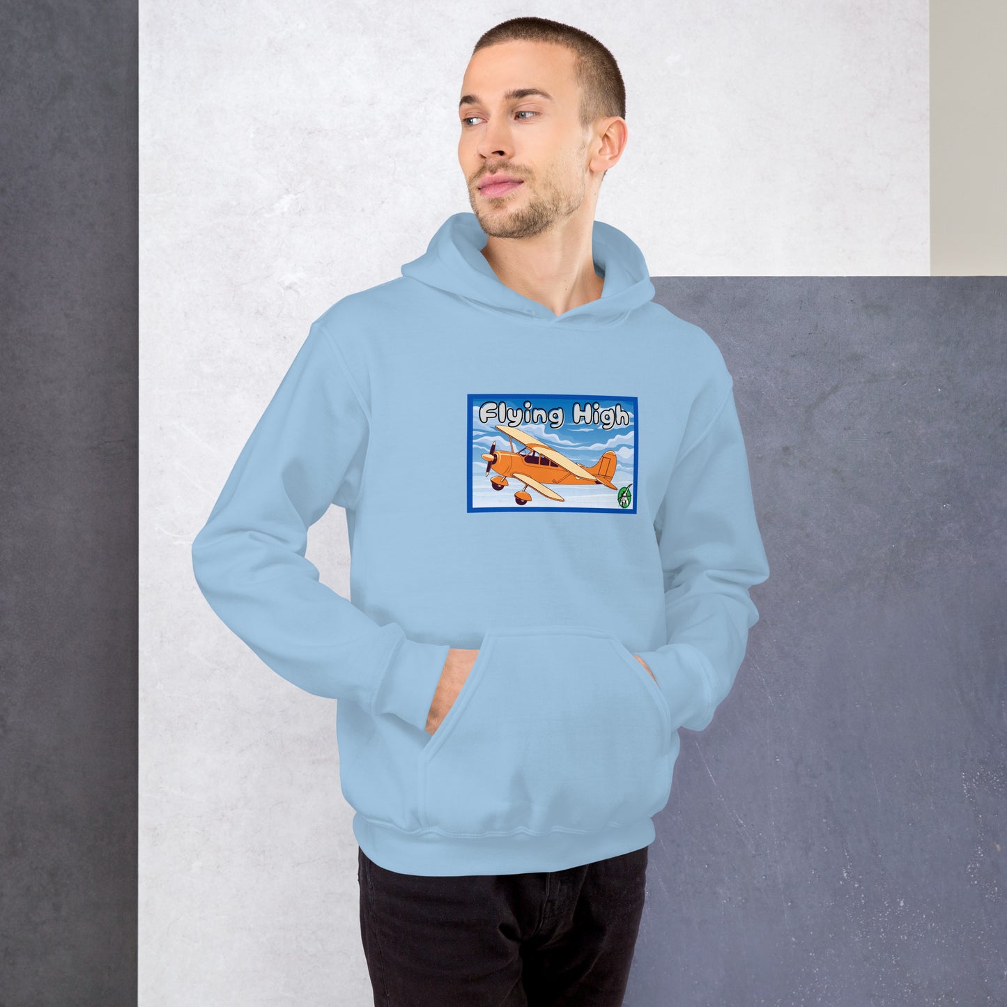 A man standing wearing a light blue hoodie with the printed graphic of a vintage airplane and the words, Flying High, by Wizard Prints.