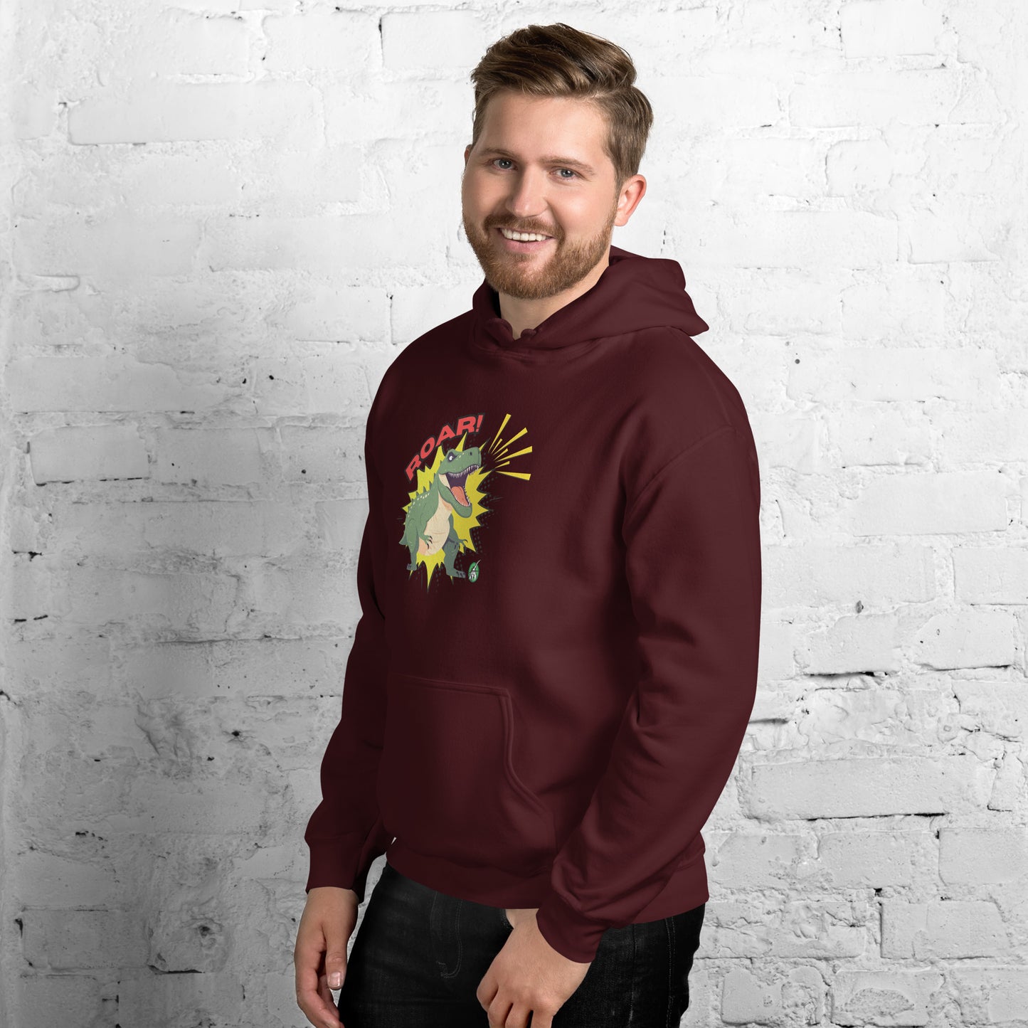 A man standing wearing a maroon hoodie with a printed graphic of a green roaring cartoon dinosaur and the word Roar! Designed by Wizard Prints