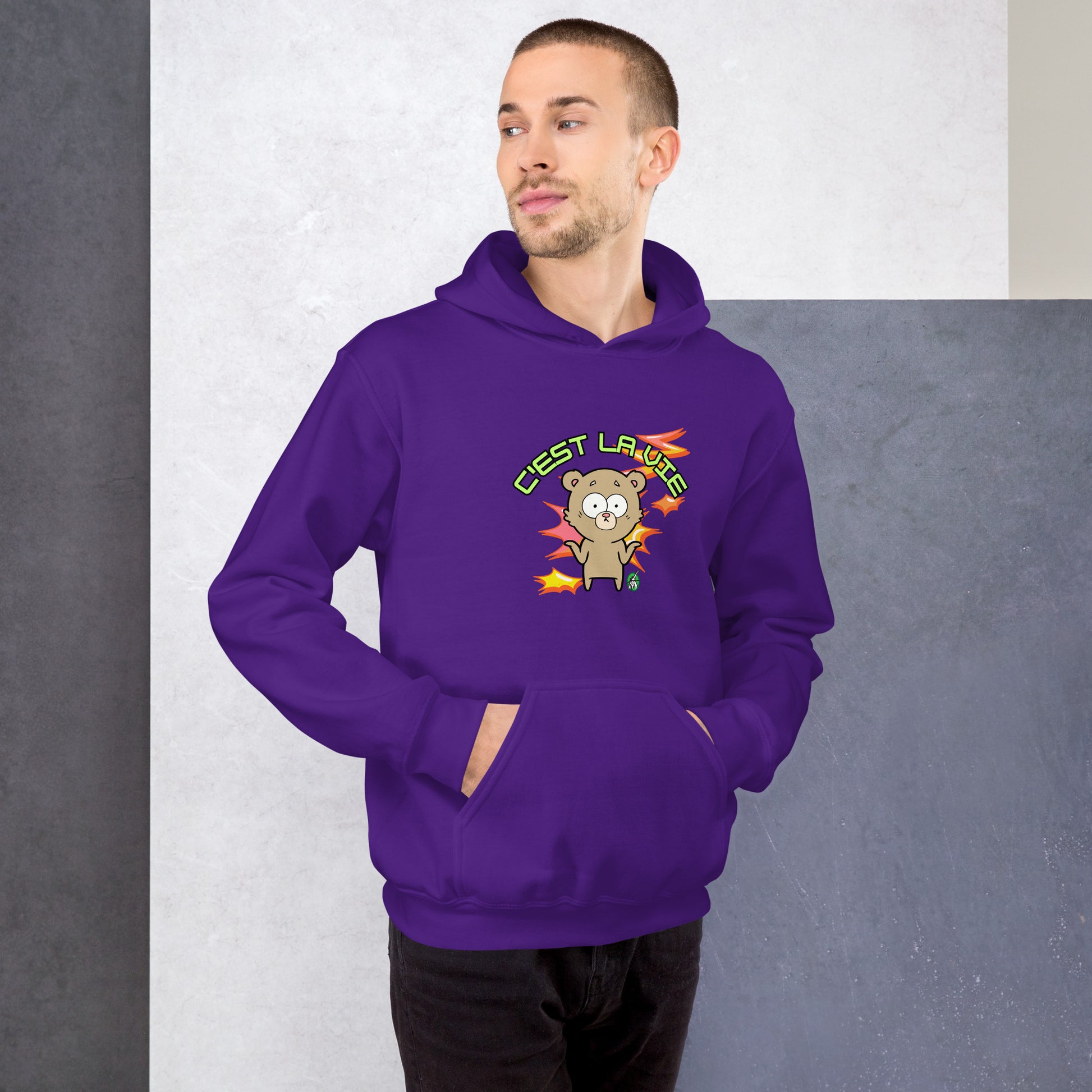 A man standing wearing a purple hoodie by Wizard Prints featuring a printed graphic of a shrugging cartoon bear and the words, C'est La Vie.