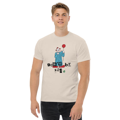A man standing and wearing a beige t-shirt with a printed graphic of a clown holding a balloon with the words, 'Don't be sad'. Designed by Wizard Prints.