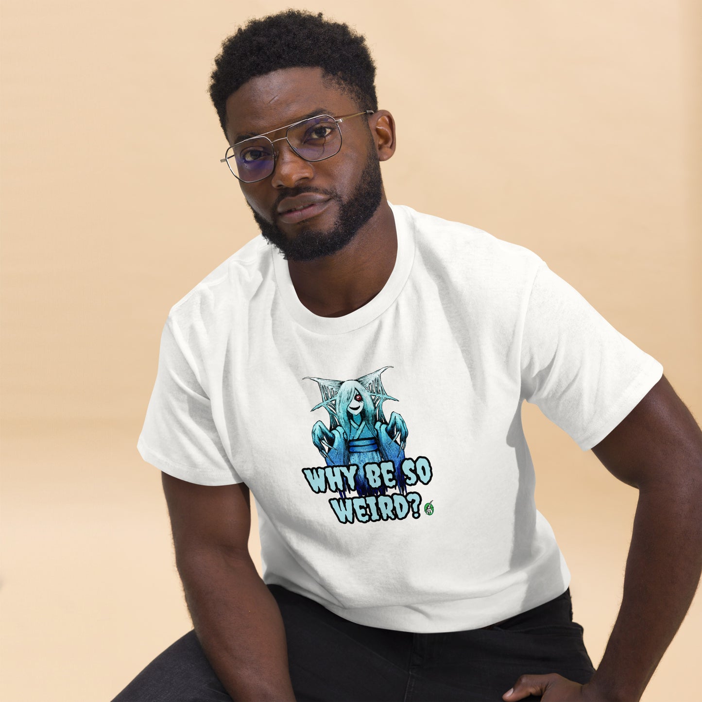 A man sitting and wearing a white t-shirt with a printed graphic of a blue ghost girl with the words, 'Why Be So Weird?'. Designed by Wizard Prints.