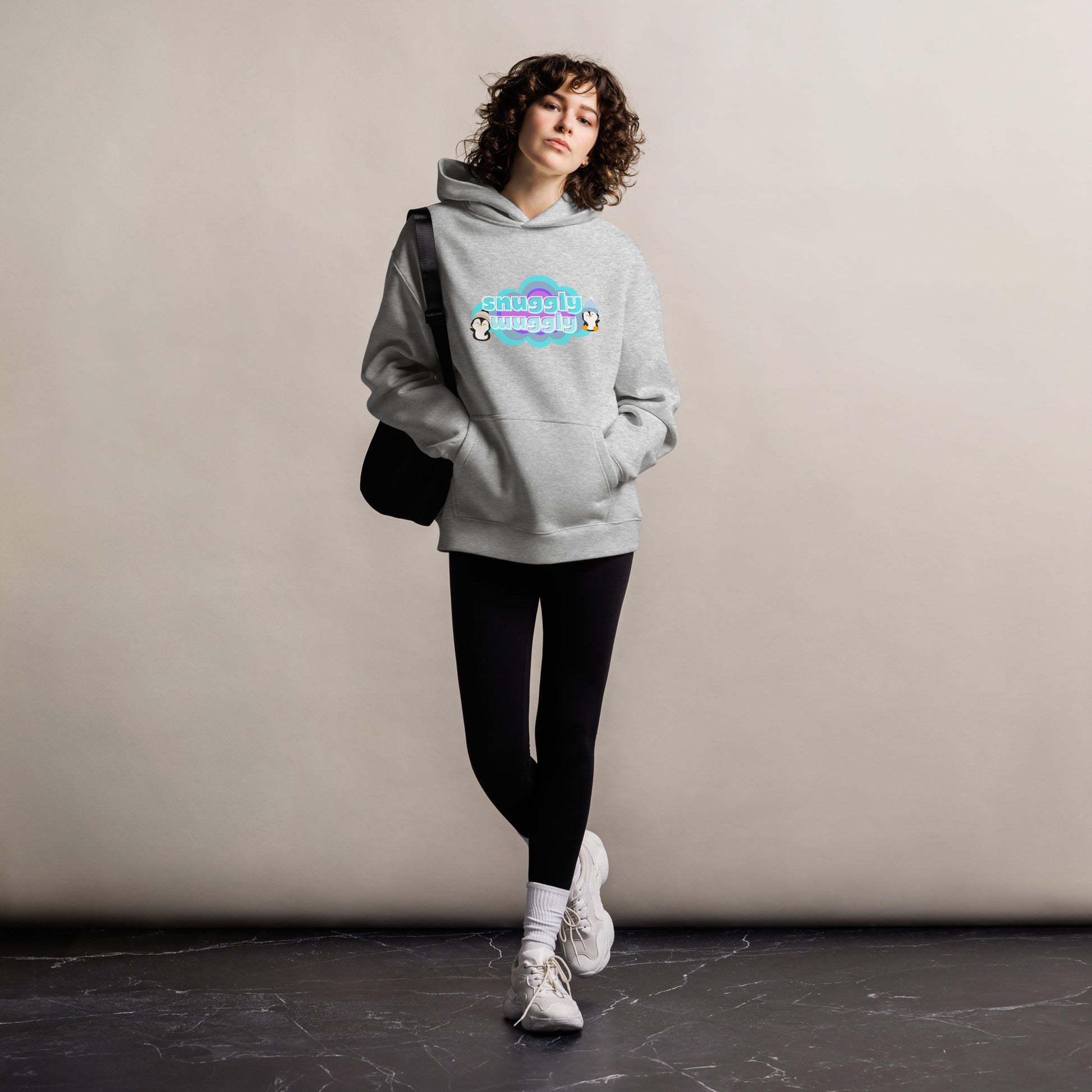 Lady standing wearing a grey hoodie with a graphic print of a couple of pequins in a cloud with the words, snuggly wuggly