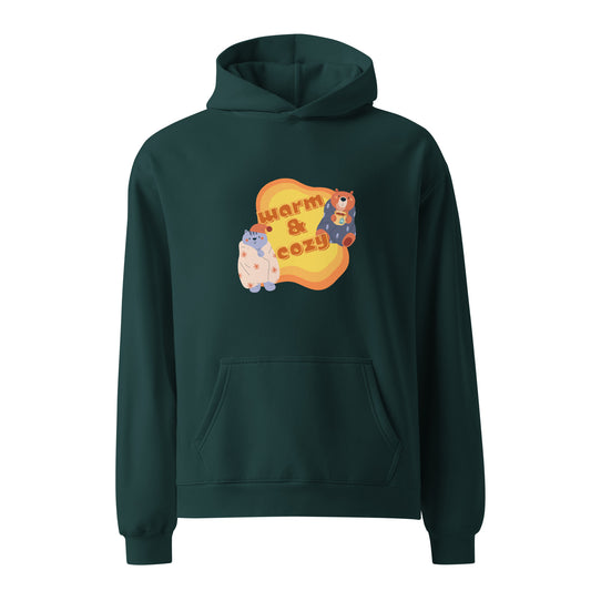 A unisex pine green hoodie by Wizard Prints featuring a printed graphic of a cartoon cat and bear wrapped in blankets and the words, Warm & Cozy. 